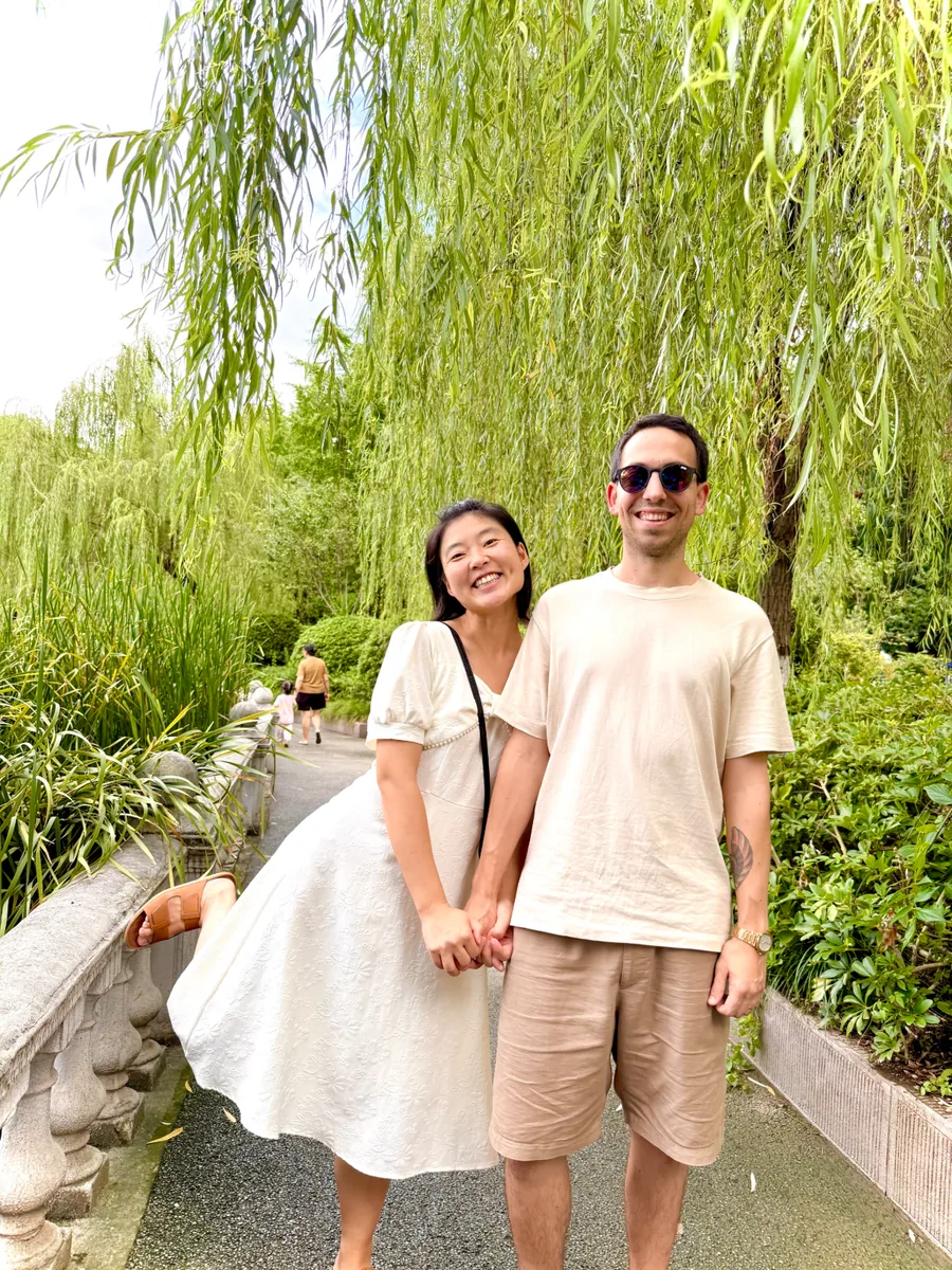 Yuan and Lucas hand in hand under willow trees